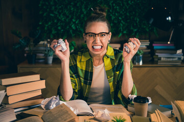 Young student with blond hair in a checkered shirt looking frustrated while studying late at home,...