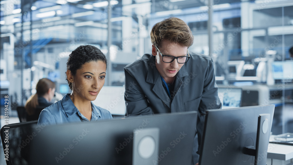 Poster Portrait of a Young Male Assembly Line Worker and Hispanic Female Engineer Collaborating on a Project, Using Computer and Talking in a Factory with Robotic Arms Producing Modern High-Tech Devices.