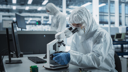 Two Scientists In Sterile Suites At Electronics Factory: Engineer Using Microscope And Desktop...