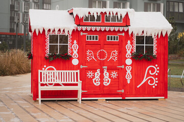 A festive red wooden house decorated with white patterns, Christmas garlands, and snow accents,...