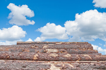 a mountain of wooden logs against a blue sky with clouds