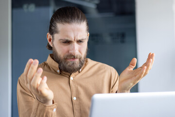 A man looks perplexed as he gestures toward his laptop, reflecting confusion at work.