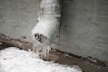 metal downspout on a building, filled with ice. The contrast of cold metal and frozen water highlights the harshness of winter and the beauty of nature's formations