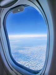Fototapeta premium A stunning airplane window view showcasing the blue sky and patterned clouds, ideal for travel, adventure, or aviation-related designs.
