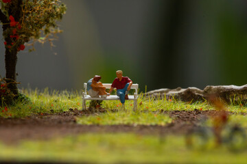 Miniature people figurine couple dating at outdoor park scenery, recreating natural morning golden light, natural background