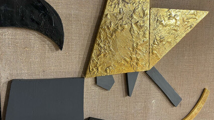 Modern abstract art close-up with textured gold, black, and gray elements on a beige burlap fabric...