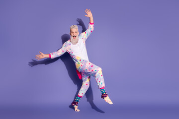 Joyful man in colorful unicorn pajama leaping against purple background