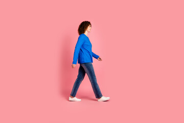 Young woman with curly hair walking confidently against a vibrant pink background in casual outfit...