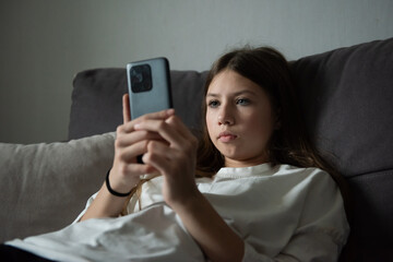 A sad teenage girl is lying with a smartphone in the dark. Sadness, problems. The concept of myopia.