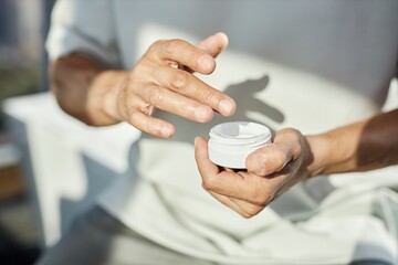 Close up on hands of mature man holding plastic jar of beauty cream applying nourishing product on...