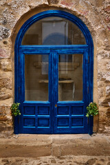 Fototapeta premium Vibrant blue door set against a rustic stone wall with potted plants