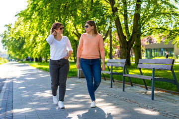Obraz premium Two mature beautiful women walking and talking in city park on spring day