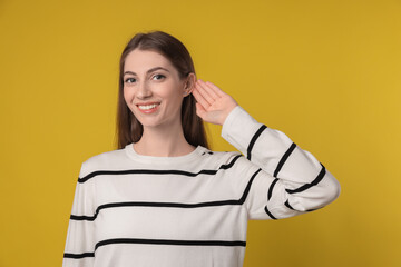 Woman showing hand to ear gesture on dark yellow background