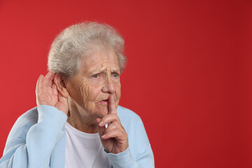 Senior woman showing hand to ear gesture on red background, space for text