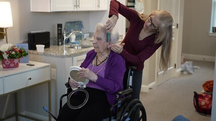 A caregiver styles the hair of an elderly woman in a wheelchair within a cozy assisted living apartment. They enjoy the moment in a warm atmosphere.