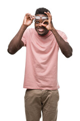 Fototapeta premium Young african american man wearing pink t-shirt doing ok gesture with hand smiling, eye looking through fingers with happy face.