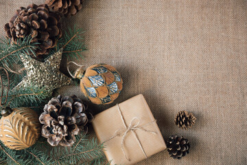A gift wrapped in paper is placed on a burlap background, surrounded by Christmas beautiful decorations. Copy space. Vintage style.
