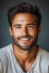 Obraz premium Smiling man with dark hair and beard wearing a casual gray shirt against a muted background enjoying a moment of happiness