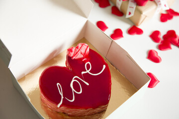 A heart-shaped cake with the inscription "Love" as a symbol of affection is placed in a box on the table. The theme is Valentine's Day.