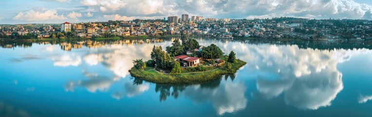 Obraz premium A picturesque drone view of the serene waters of Lake Anosy in Antananarivo, featuring the small island in the center with its lush vegetation The city skyline in the background adds a cultural touch
