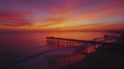 Obraz premium Colorful sunset over the Pacific Ocean illuminating a long pier filled with visitors enjoying the tranquil beach atmosphere
