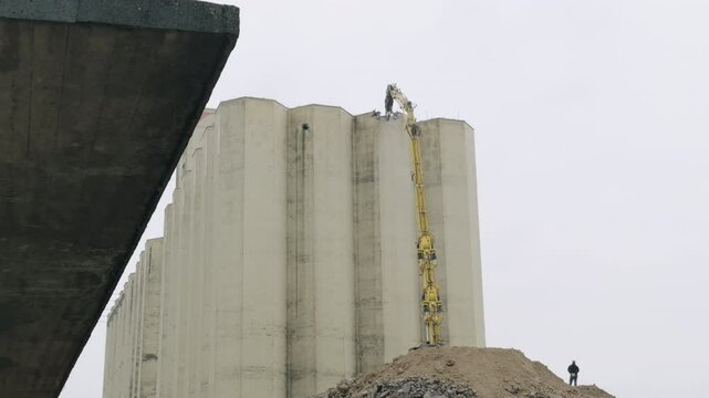 Demolition crane slowly breaking industrial silo from the top 4K