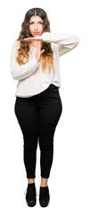 Young beautiful woman wearing white sweater Doing time out gesture with hands, frustrated and...