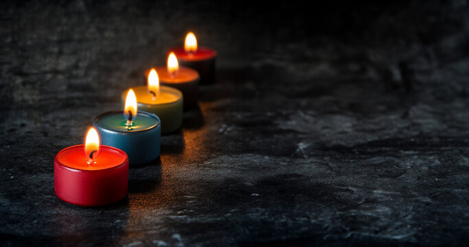Multi colored tea light candles in a row on a dark background with room for text. 