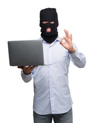 Business hacker man holding a computer laptop doing ok sign with fingers, excellent symbol