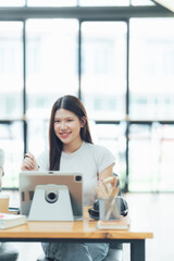 Obraz premium Focused and Inspired: A young woman, radiating positivity, works on a tablet in a modern office setting, showcasing the power of technology and creativity. 