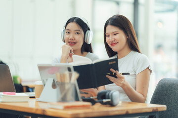 Obraz premium Two friends studying together, smiling at each other, sharing knowledge and support in a cozy cafe setting. The image evokes a sense of collaboration, learning, and shared joy. 