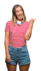 Fototapeta premium Young beautiful woman listening music wearing headphones over isolated background smiling with happy face looking and pointing to the side with thumb up.