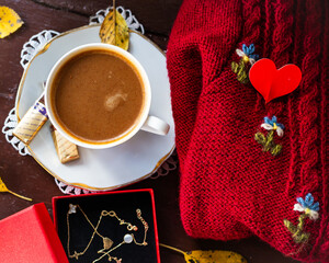 scena autunnale con una tazza di caffe, un maglione, una collana e un cuore rosso