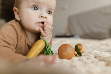 Adorable happy baby boy playing with wooden toys on bed. Safe Childhood. Portrait of cute child infant teething with eco toys
