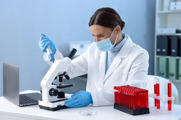 Laboratory testing. Doctor dripping blood sample onto glass slide while working with microscope at...