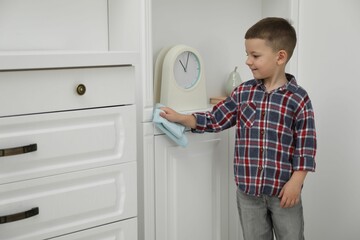 Little helper. Cute boy wiping dust from furniture at home