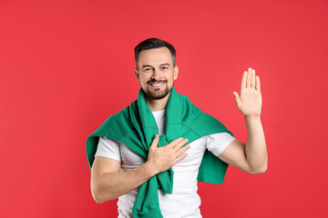 Man making promise with raised hand on red background. Oath gesture