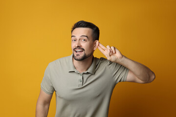 Man showing hand to ear gesture on orange background