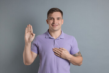 Man making promise with raised hand on grey background. Oath gesture