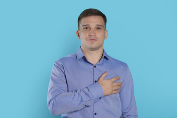 Man making promise on light blue background. Oath gesture