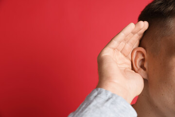 Man showing hand to ear gesture on red background, closeup. Space for text