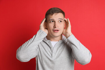 Man showing hand to ear gesture on red background
