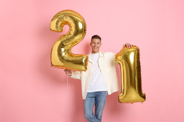 Coming of age party - 21st birthday. Happy young man with number shaped balloons on pink background