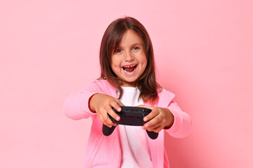 Fototapeta premium Happy little girl playing video game with controller on pink background