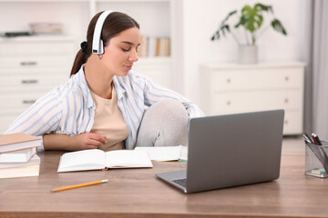 Student in headphones studying at wooden table indoors
