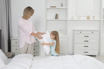 Obraz premium Little girl helping her mother making bed at home