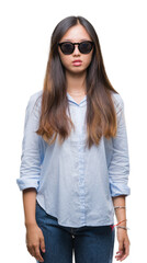 Naklejka premium Young asian woman wearing sunglasses over isolated background with serious expression on face. Simple and natural looking at the camera.