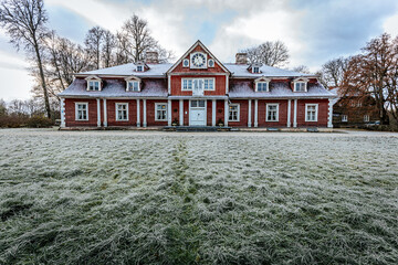 A picturesque view of Ungur Manor, a historical red wooden building with frosted grass in the...