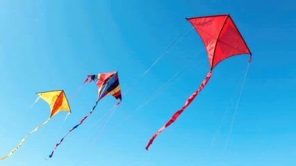 Three brightly colored kites of different sizes fly gracefully in a clear, sunny sky. Concept of freedom, fun, or summer activities.
 