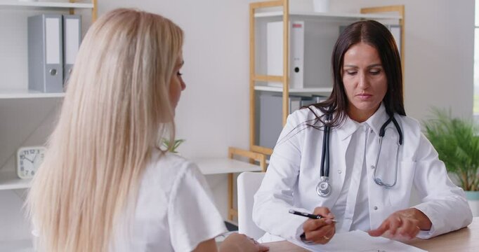 Friendly smiling practitioner explaining the treatment plan while writing down the prescription and giving it to the female patient. Two happy women shake hands after a successful medical consultation